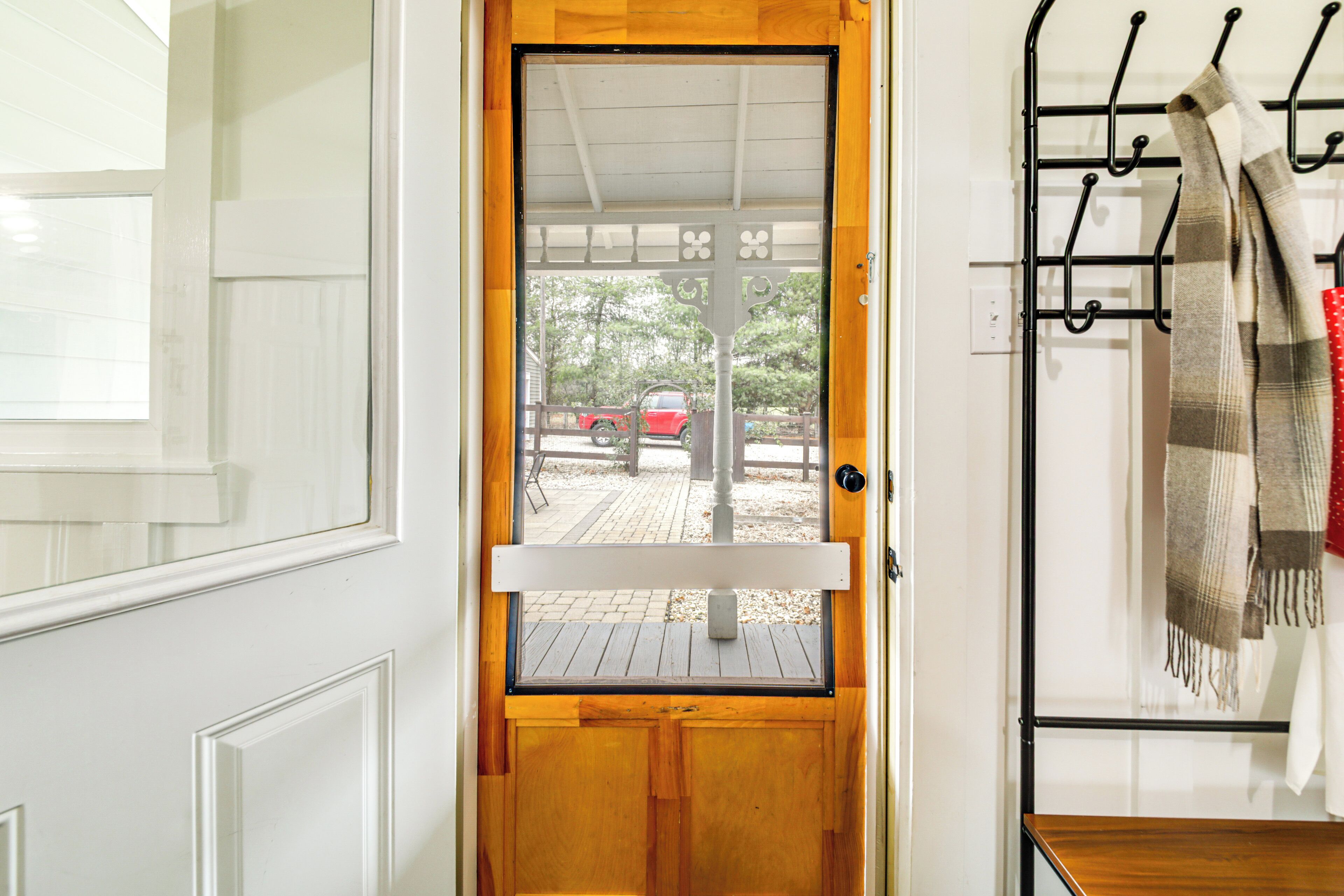 Une porte en bois avec un panneau de verre, un porte-manteau en métal sur lequel est posé un foulard, et une vue sur un véhicule rouge à l’extérieur.