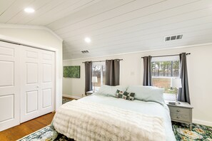 A bedroom with a large bed, a nightstand, a dresser, and a window with curtains.