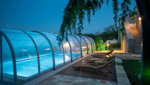 Una piscina rodeada de vidrio con sillas de descanso y una terraza de madera.