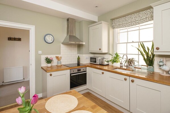 A kitchen with white cabinets, a microwave, a stove, and a window with plants.