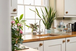 A kitchen with white cabinets, a wooden countertop, a sink, and various kitchen items including a kettle and a dish soap dispenser.