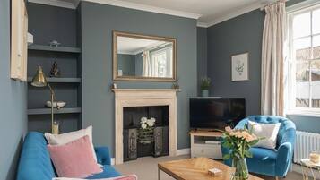 A living room with a blue sofa, a fireplace, a television, and a window with curtains.