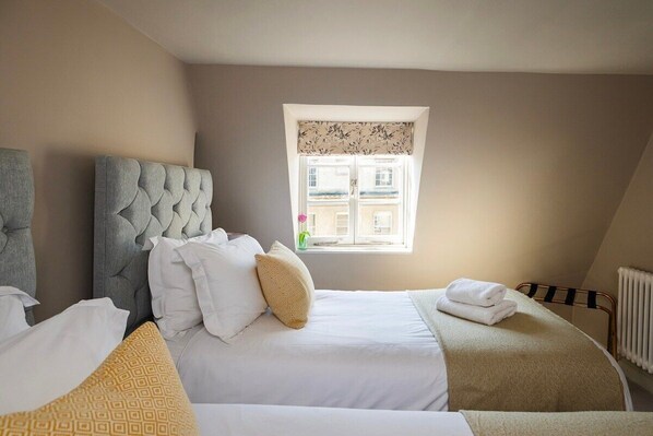 A bedroom with two beds, a window with a view of buildings, and a radiator. - Stylish Georgian Apartment in Centre of Bath (Bath)