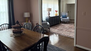 A dining area with a wooden table and chairs, a sideboard with a lamp, and a view into a living room through an open doorway. - Sleeps 10 close to all attractions! BMSpeedWay, DT, Casino, Holston & Boone Lake (Bristol)