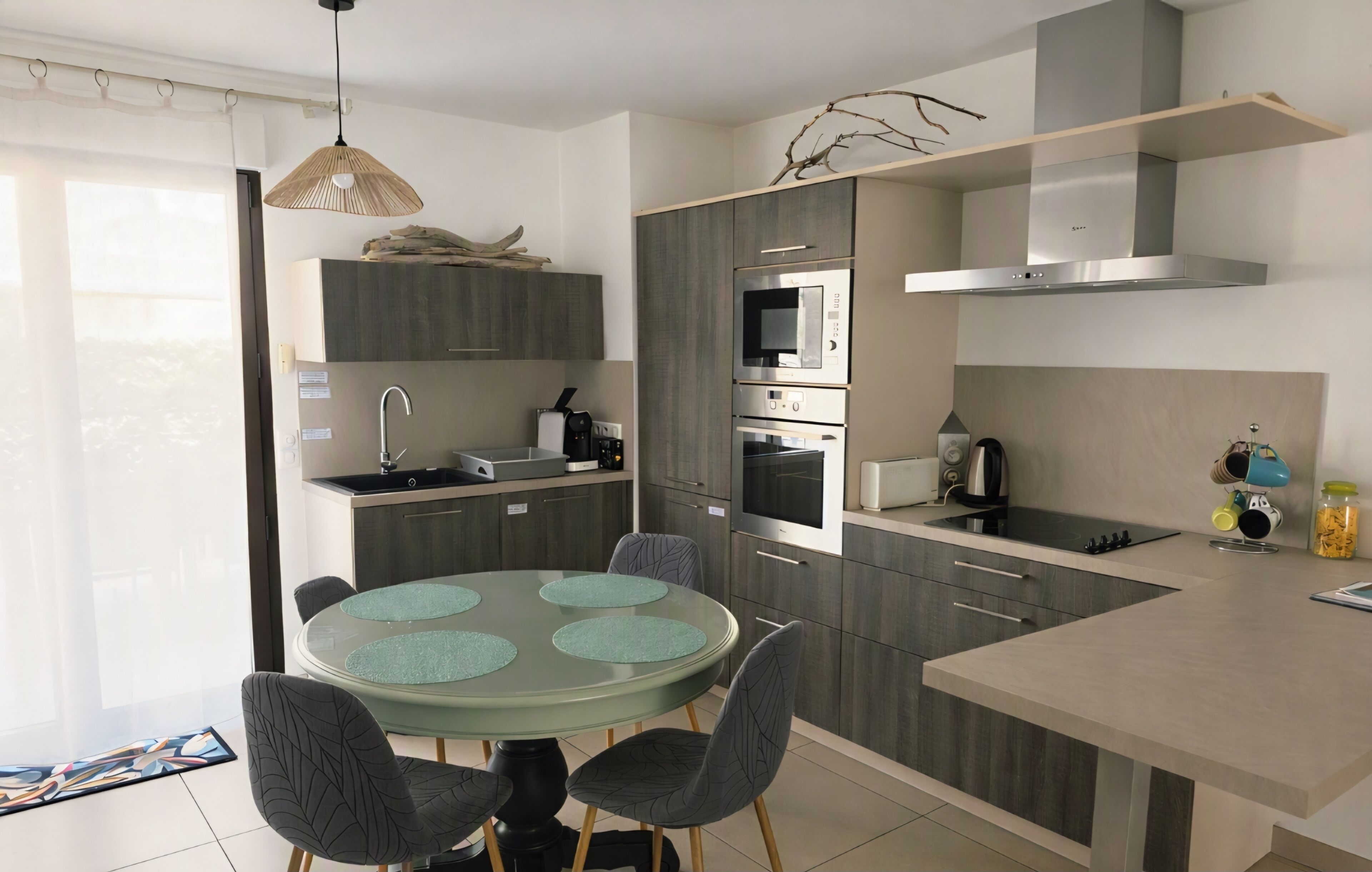 Une cuisine moderne avec une table de salle à manger ronde, des appareils électroménagers intégrés et un luminaire suspendu.