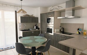 Een moderne keuken met een ronde eettafel, inbouwapparatuur en een hanglamp.