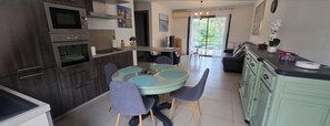 Une cuisine moderne avec un coin repas, comprenant une table ronde avec des chaises, un four encastré et une vue sur un balcon.
