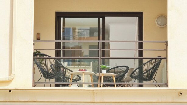 Een balkon met een tafel, stoelen, een raam en een deur.