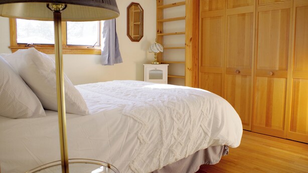 A bedroom with a bed, a lamp, a dresser, a mirror, and a wooden wardrobe. - Spacious Lakeside house on Long Lake Saint Agatha! (Saint Agatha)