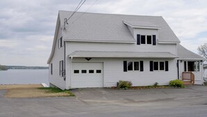 A two-story house with a garage, a small porch, and a view of a body of water. - Spacious Lakeside house on Long Lake Saint Agatha! (Saint Agatha)