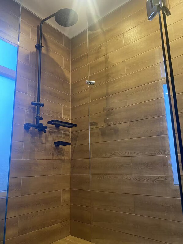 A shower with a wooden panel wall, a handheld showerhead, and a handheld shower attachment.