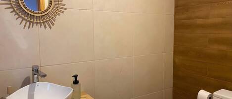 A bathroom with a white sink, a mirror with a sunburst frame, a soap dispenser, and a toilet.