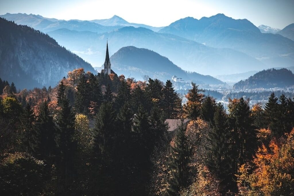 Bergachtig landschap met een kerktoren, dicht bos en een in de verte gelegen stad.
