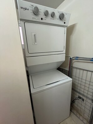 A Whirlpool washer and dryer stacked in a laundry room with a metal rack and a tiled wall. - BeachFront Apartament - Private Beach Access (Punta Cana)
