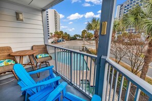 A balcony with wicker furniture and a view of a pool and palm trees. - Bluewater Resort V110A – Your Myrtle Beach Getaway (Myrtle Beach)