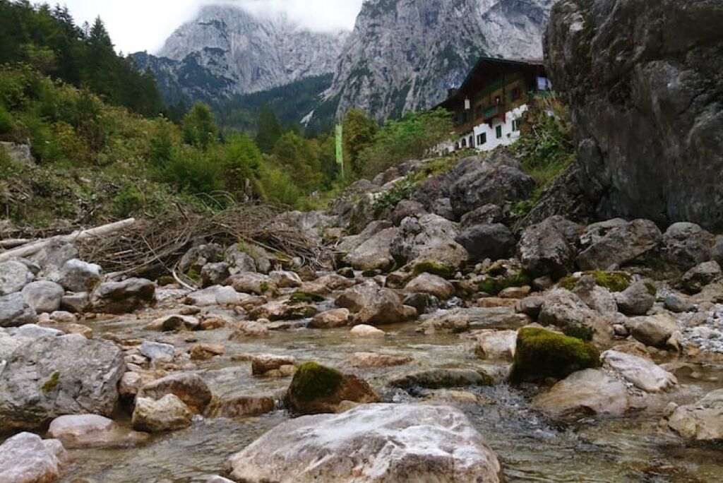 A rocky stream with a house on a mountain slope.