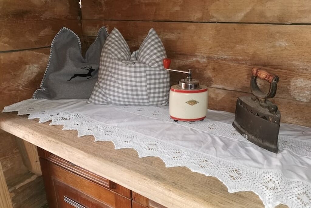 A wooden table with a lace tablecloth, a vintage can opener, a checkered pillow, and a decorative pillow with a tree design.