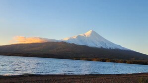 Une montagne enneigée se dressant sous un ciel dégagé, avec une étendue d'eau calme au premier plan.