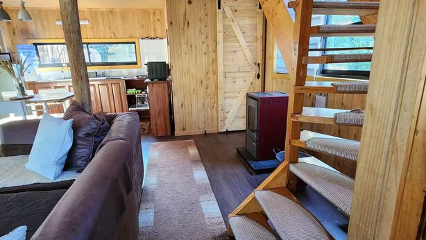 L’intérieur d’un chalet confortable, avec un escalier en bois, un canapé et un téléviseur.
