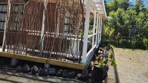 Une maison dotée d’un porche abrité, d’une terrasse en bois et d’un jardin où poussent différentes espèces de plantes.