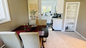 A dining area with a table, chairs, and a kitchen in the background. - Location! Location!  Bright, modern and clean south Oak Bay garden suite. (Victoria)