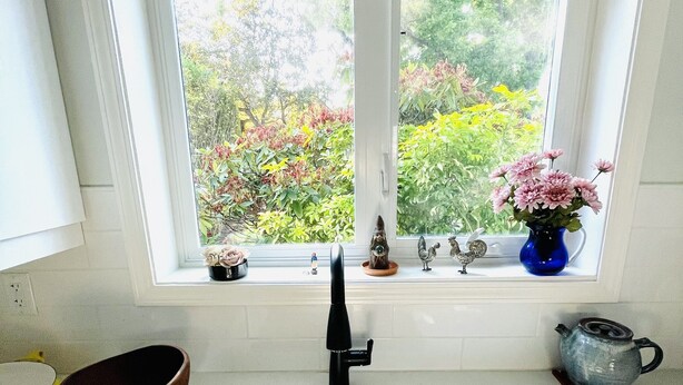 A kitchen with a black sink, a window with a view of greenery, and a vase with flowers on the windowsill. - Location! Location!  Bright, modern and clean south Oak Bay garden suite. (Victoria)