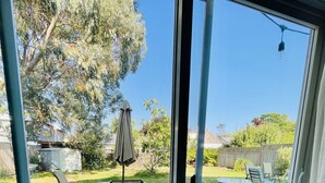 A patio area with outdoor furniture, a trash bin, and a view of a backyard with trees and a fence. - Location! Location!  Bright, modern and clean south Oak Bay garden suite. (Victoria)