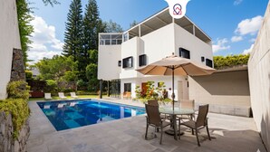 A modern two-story house with a swimming pool, outdoor furniture, and a patio area.