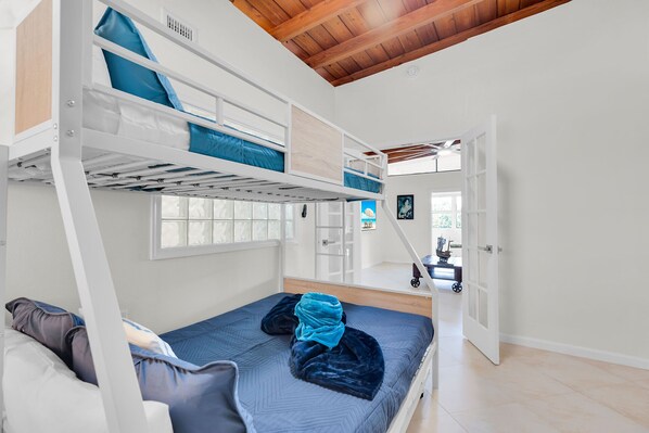 A bunk bed room with a loft bed, a window, and a door leading to another room. - Marathon Beach House | Pool, Dock & Ocean Views (Marathon)