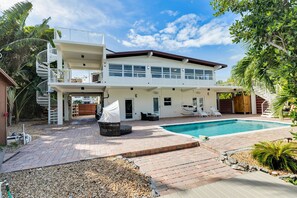 A two-story house with a swimming pool, outdoor seating, and a staircase leading to a balcony. - Pet Friendly! Ocean Views, Pool & Dock | Walk to Sombrero Beach 🏖️ (Marathon)