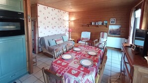 L’intérieur chaleureux d’un chalet comprend une table à manger pour quatre personnes, un canapé, un téléviseur et un coin cuisine.