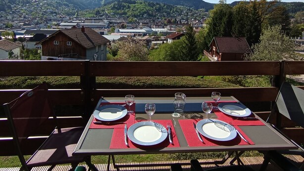 Un espace de restauration en plein air avec une table dressée pour deux personnes, offrant une vue panoramique sur une ville et des collines.