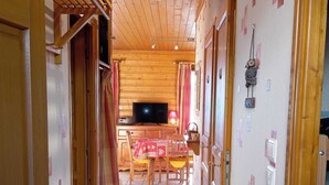 Un couloir aux murs et au plafond en bois, qui mène à une salle à manger avec une table et des chaises.