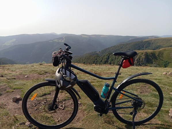 Un vélo est garé sur une colline herbeuse, offrant une vue panoramique sur les montagnes en arrière-plan.
