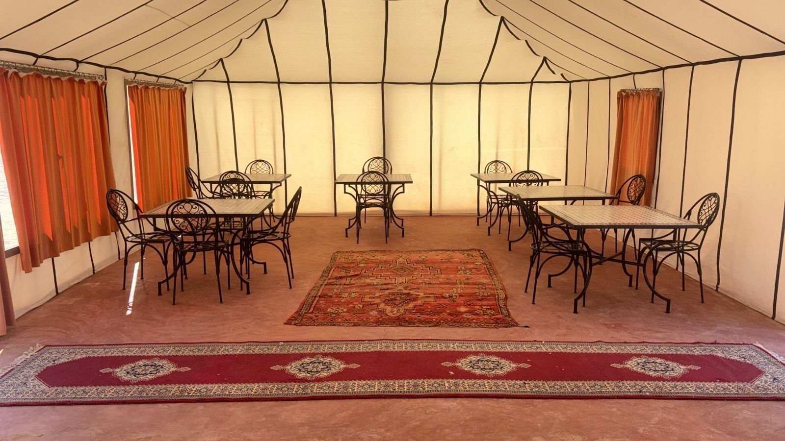 Un área de comedor con carpas, mesas y sillas, una alfombra central y cortinas.