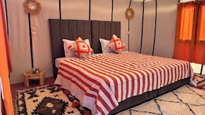 A bedroom with a striped bedspread, two pillows with geometric patterns, a dark headboard, and a patterned rug.