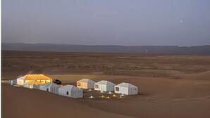 A desert landscape with several tents and a large, illuminated structure.