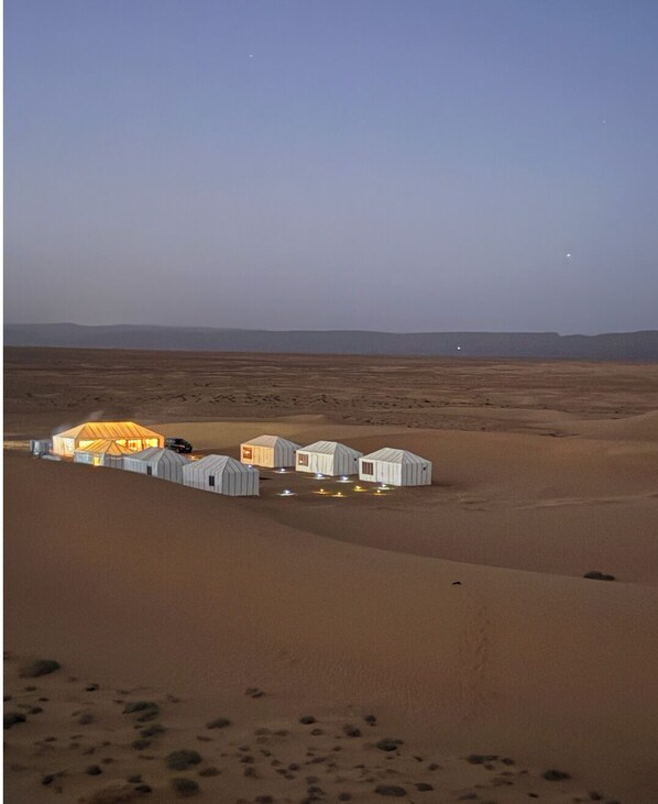 A desert landscape with several tents and a large, illuminated structure.