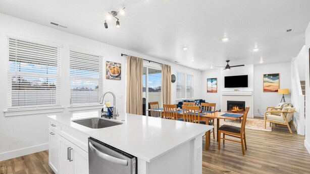 Una cocina moderna con una isla central, zona de comedor con sillas de madera, chimenea y televisor montado en la pared.