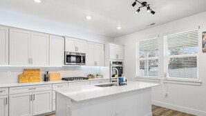 Una cocina moderna con armarios blancos, una isla central, microondas, horno y fregadero.