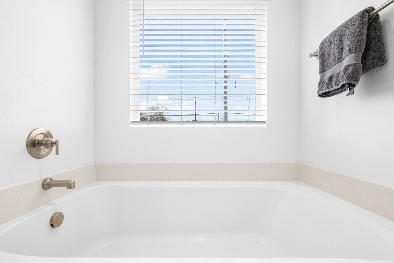 A bathroom with a bathtub, a window with blinds, a towel rack, and a faucet.