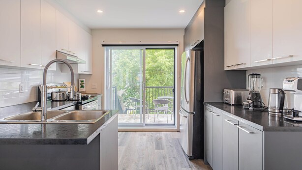 Una cocina moderna con una isla grande, electrodomésticos de acero inoxidable y un ventanal corredero que da a un balcón.