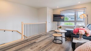 Una sala de estar moderna con una escalera de madera, un televisor de pantalla plana, un sofá, una mesa de centro y una ventana con vistas al exterior.