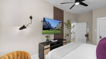 A modern hotel room with a bed, a television mounted on the wall, a ceiling fan, and a small plant on the nightstand.