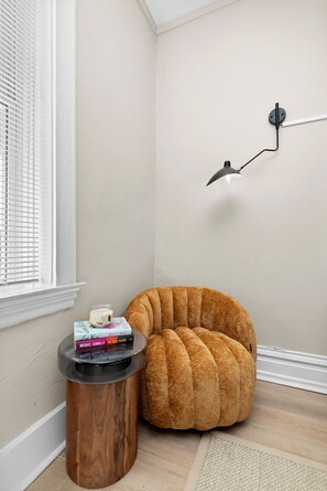 A corner room with a round, upholstered chair, a small wooden side table, and a wall-mounted lamp. - Lovely 1-bedroom house with AC in charming St. Louis (St. Louis)
