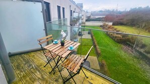 A modern balcony with a wooden table and chairs, a glass railing, and a view of a green landscape. - Warm&Bright 1BR w terrace&parking (Luxembourg City)