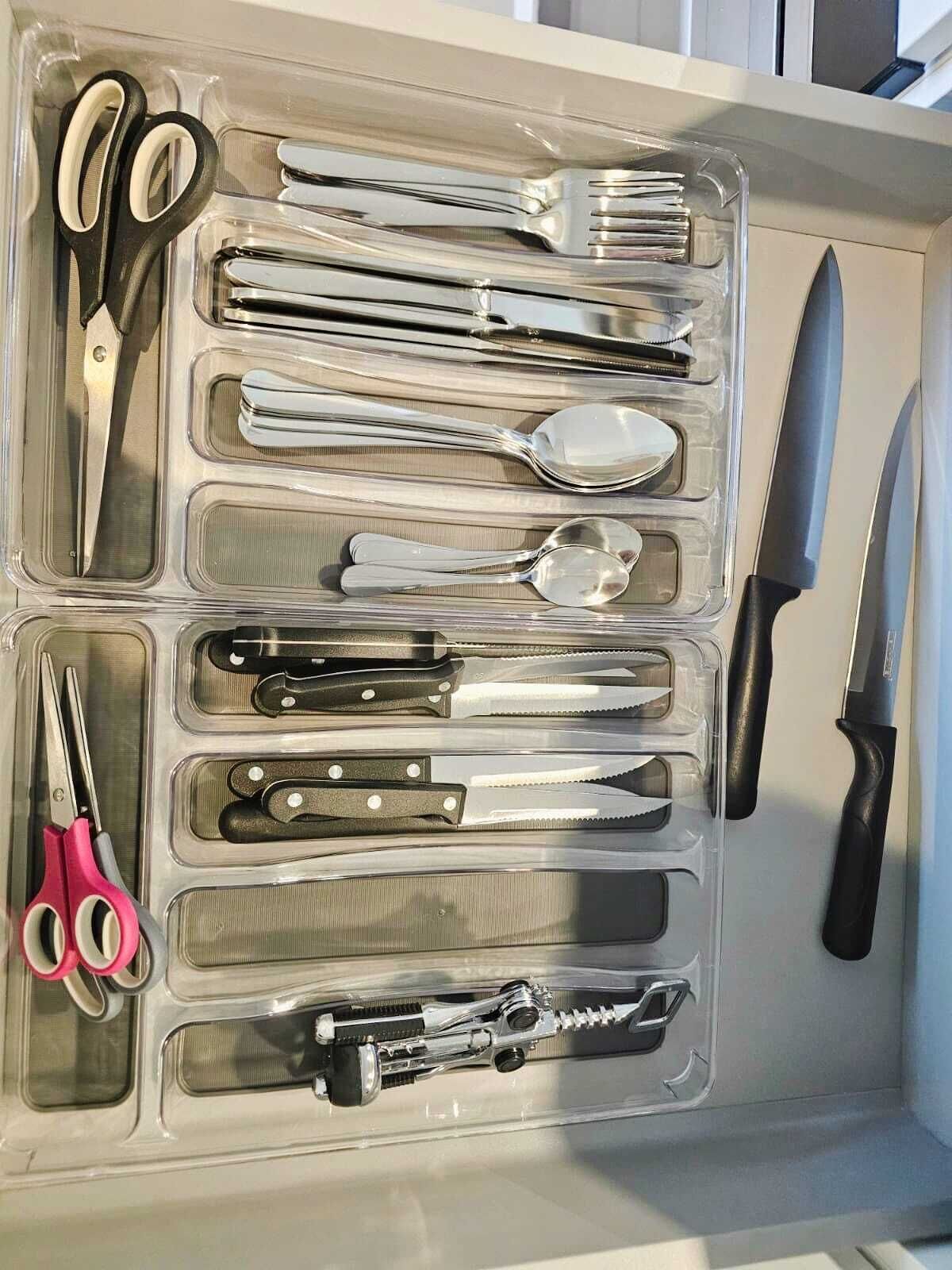 Eine Schublade mit verschiedenen Küchenutensilien, darunter Scheren, Löffel, Gabeln, Messer und eine Zange.
