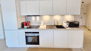 A modern kitchen with white cabinetry, a built-in oven, a microwave, and a sink. - Warm&Bright 1BR w terrace&parking (Luxembourg City)