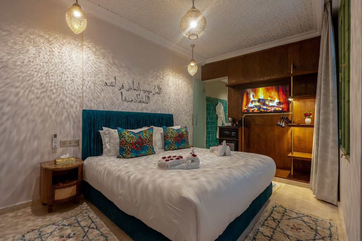 A hotel room with a large bed, teal curtains, a wall-mounted TV, and a wooden cabinet.