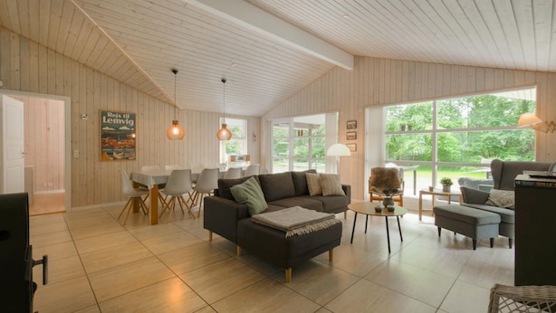 Un vaste espace de vie comprenant une grande fenêtre, une table à manger avec des chaises, un canapé et une petite table agrémentée d’objets décoratifs.